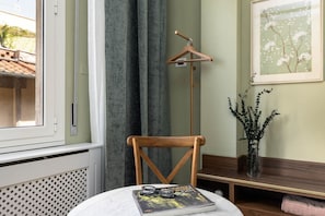 Ein Zimmer mit einem Holzstuhl, einem Tisch mit Zeitschrift und Gläsern, einem an der Wand befestigten Kleiderhaken, einem gerahmten Bild und einer Pflanzvase.
