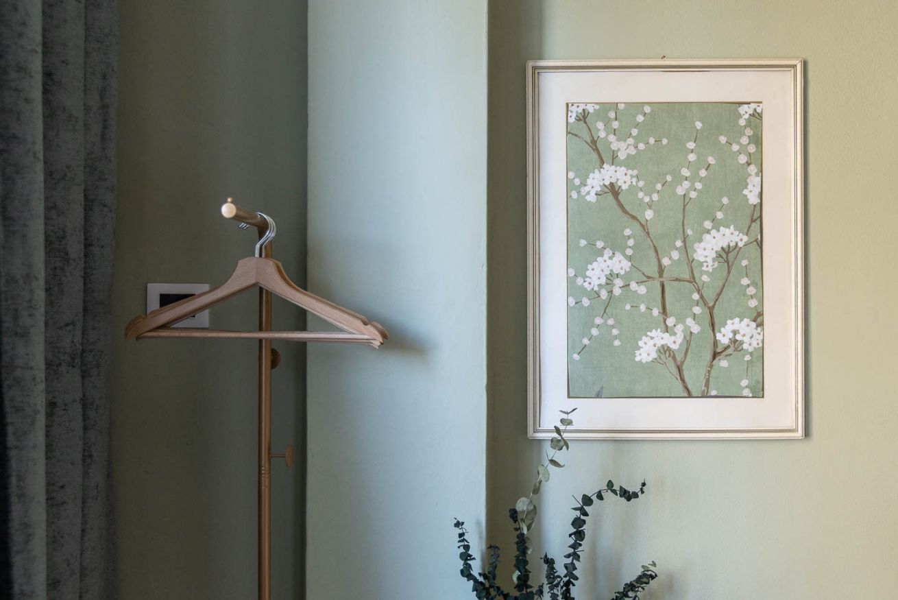 Une œuvre d’art encadrée représentant des fleurs blanches sur un mur, un cintre en bois et une plante aux feuilles sombres.