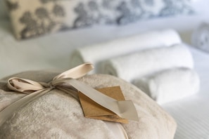 Ein ordentlich verpacktes Geschenk mit Schleife, platziert auf einem Bett mit Kissen und einem gemusterten Kissen im Hintergrund.