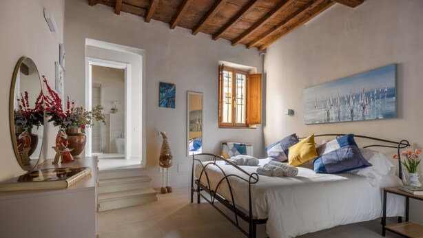 A bedroom with a bed, a dresser, a mirror, a window, and a painting on the wall. - Dimora Camaldoli - Authentic Florence Experience (Firenze)