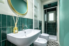 Ein Badezimmer mit weißem Waschbecken, einem Spiegel, einer Toilette und einer Duschkabine.