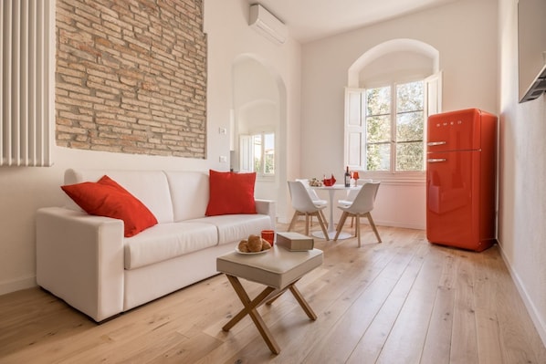 A modern living room with a white sofa, red cushions, a small table, and a red refrigerator. - Boboli Dreams- Luxury in the Historic Heart of Florence (Firenze)