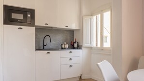 A compact kitchen with white cabinets, a Bosch microwave, a black faucet, and a window with blinds. - Boboli Dreams- Luxury in the Historic Heart of Florence (Firenze)