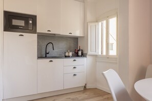 A compact kitchen with white cabinets, a Bosch microwave, a black faucet, and a window with blinds. - Boboli Dreams- Luxury in the Historic Heart of Florence (Firenze)