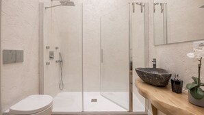 A modern bathroom with a glass-enclosed shower, a white toilet, and a wooden vanity with a large bowl sink. - Boboli Dreams- Luxury in the Historic Heart of Florence (Firenze)