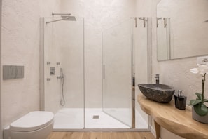 A modern bathroom with a glass-enclosed shower, a white toilet, and a wooden vanity with a large bowl sink. - Boboli Dreams- Luxury in the Historic Heart of Florence (Firenze)