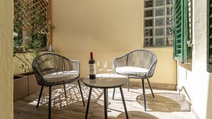 A small patio with two wicker chairs, a round table, a bottle of wine, and two wine glasses. - Augustus Florence Borgo Pinti 3 min Duomo (Firenze)