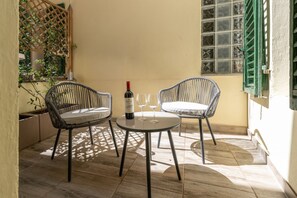 Eine kleine Terrasse mit zwei Korbstühlen, einem runden Tisch, einer Weinflasche und zwei Weingläsern.