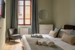 Ein Hotelzimmer mit Bett, Sessel, Kommode, rundem Spiegel und einem Fenster mit Vorhängen.