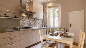 A modern kitchen with a dining area, featuring a gas stove, a sink, and a window with curtains. - Augustus Florence Borgo Pinti 3 min Duomo (Firenze)