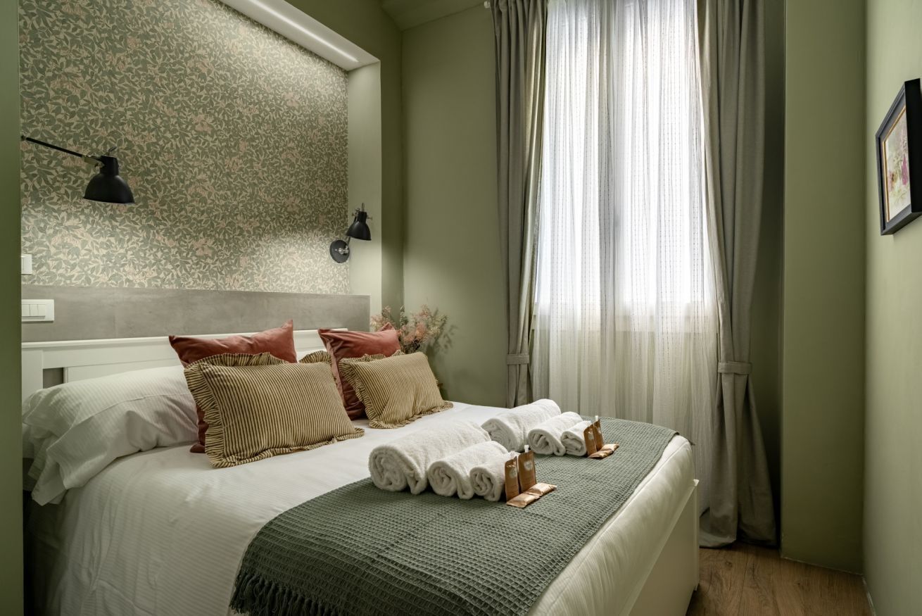 Een opgemaakt bed met opgerolde handdoeken, een hoofdbord en een behang met een patroon.