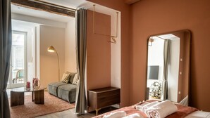 Ein Hotelzimmer mit Bett, Nachttisch, Sofa, kleinem Tisch, Lampe, Spiegel und Blick ins Freie.