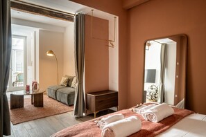 Ein Hotelzimmer mit Bett, Nachttisch, Sofa, kleinem Tisch, Lampe, Spiegel und Blick ins Freie.