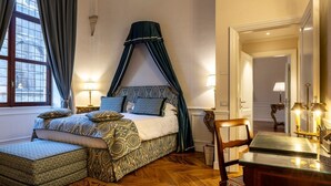 A bedroom with a canopy bed, a bedside table, a chair, and a desk with a lamp. - The Loggia of Borgo SS Apostoli (Firenze)