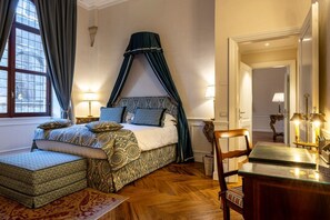 Ein Schlafzimmer mit Baldachinbett, Nachttisch, Sessel und Schreibtisch mit Lampe.