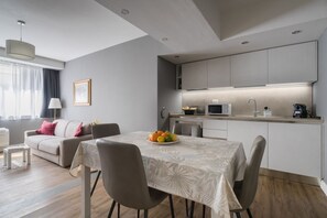 Ein modernes Wohnzimmer mit Essbereich, einer Küche mit Einbaugeräten und einem großen Fenster mit Vorhängen.