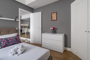 Ein modernes Schlafzimmer mit einem Bett, einem Nachttisch, einer Kommode, einem Kleiderschrank und einer Küchenzeile im Hintergrund.