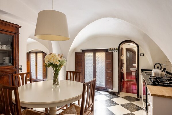 A dining area with a round table, chairs, a vase with flowers, a hanging light fixture, and a kitchen with a stove and sink. - The Renaissance Chapel by Maison Florence (Florence)