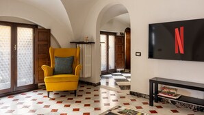 Eine Hotellobby mit einem gelben Sessel, einem Fernseher mit rotem ‚N‘-Logo, einem Schachbrettfußboden und gewölbten Decken.