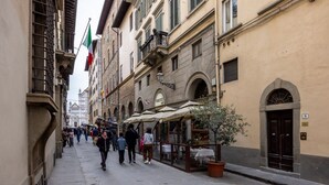A narrow street with buildings, outdoor seating, and flags. - Santa Croce Historic Apartment by Maison Florence (Florence)