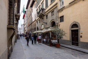 A narrow street with buildings, outdoor seating, and flags. - Santa Croce Historic Apartment by Maison Florence (Florence)