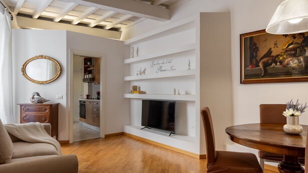 A living room with a fireplace, a dining table with chairs, a sofa, a TV, and a kitchen area in the background. - Santa Croce Historic Apartment by Maison Florence (Florence)