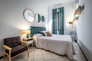 Ein Schlafzimmer mit einem Bett, einem Sessel, einem Nachttisch, einer Lampe und einem an der Wand befestigten Regal mit Pflanzen.