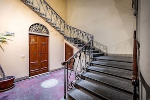 Eine Treppe mit aufwendiger Metallreling, einer Holztür und einem Blumentopf.