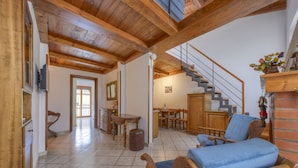 Un vaste espace de vie doté d’un plafond en bois, d’un escalier, d’un coin repas et d’un fauteuil bleu rembourré.