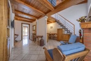 A spacious living area with a wooden ceiling, a staircase, a dining area, and a blue cushioned chair. - Romantic Home - Charm and Elegance in the Heart of Florence (Firenze)