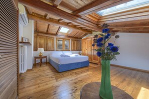 A bedroom with a wooden ceiling, a bed, a nightstand, a lamp, and a vase with flowers. - A Romantic Home—Charm and Elegance in the Heart of Florence   (Firenze)