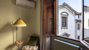 A corner room with a radiator, a window with a view of buildings, a lamp, and a chair. - Geometric Design Suite by Maison Florence (Florence)