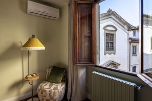 A corner room with a radiator, a window with a view of buildings, a lamp, and a chair. - Geometric Design Suite by Maison Florence (Florence)