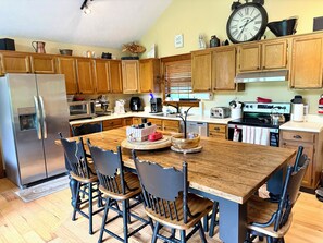 A kitchen with wooden cabinets, a stainless steel refrigerator, a wooden dining table with chairs, and a clock on the wall.