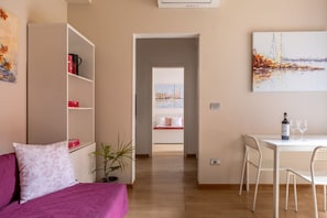 Ein modernes Wohnzimmer mit einer Couch, einem Esstisch mit Stühlen, einem Bücherregal und einem Gemälde an der Wand.