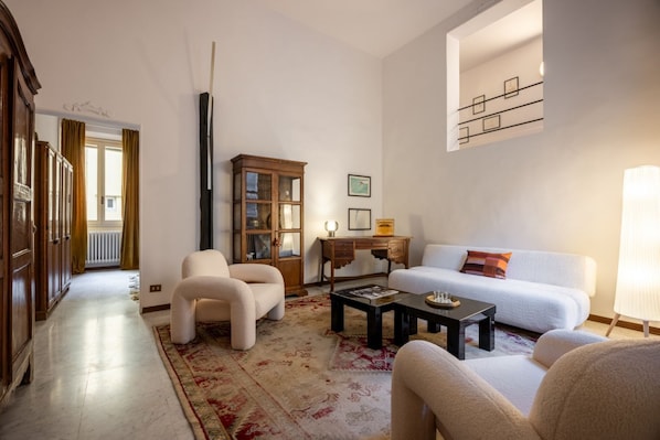 Ein Wohnzimmer mit einer Couch, Sesseln, einem Couchtisch, einem Schrank und einer Lampe.