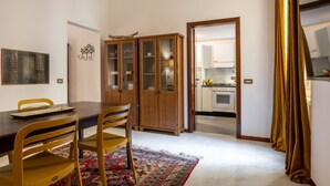 A dining area with a wooden table, chairs, and a patterned rug. There is a cabinet with glass doors and a kitchen visible through an open doorway. - Like a Local Borgo San Jacopo By Maison Florence (Firenze)