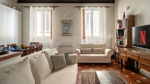 A living room with a sofa, a TV, a bookshelf, and a dining area with a table and chairs. - Borgo Pinti Medieval Apartment (Firenze)