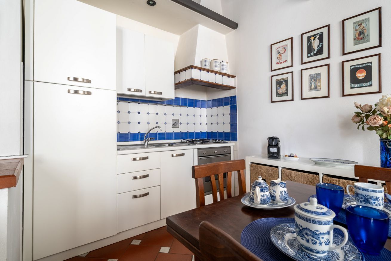 A kitchen with white cabinets, blue tiles, a coffee machine, and framed pictures on the wall.