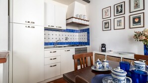 A kitchen with white cabinets, blue tiles, a coffee machine, and framed pictures on the wall. - Borgo Pinti Medieval Apartment (Firenze)
