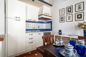 A kitchen with white cabinets, blue tiles, a coffee machine, and framed pictures on the wall. - Borgo Pinti Medieval Apartment (Firenze)