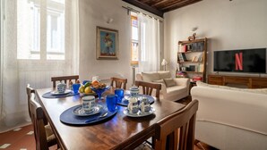 A dining area with a wooden table set for four, a sofa, a bookshelf, and a TV displaying the Netflix logo. - Borgo Pinti Medieval Apartment (Firenze)