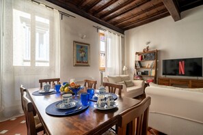 A dining area with a wooden table set for four, a sofa, a bookshelf, and a TV displaying the Netflix logo. - Borgo Pinti Medieval Apartment (Firenze)