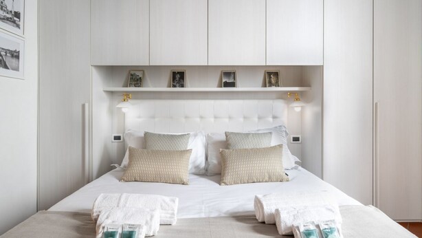 A neatly made bed with white linens, a headboard, and a shelf above it. - Borgo Pinti Medieval Apartment (Firenze)