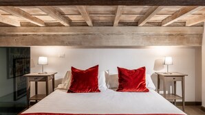 A hotel room with a wooden ceiling, a bed with white bedding and red pillows, two bedside tables with lamps, and a framed picture on the wall. - Calimaruzza Apartment - by Maison Florence (Firenze)