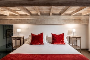 A hotel room with a wooden ceiling, a bed with white bedding and red pillows, two bedside tables with lamps, and a framed picture on the wall. - Calimaruzza Apartment - by Maison Florence (Firenze)