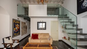A modern living room with a sofa, a coffee table, a glass staircase, and a chandelier. - Calimaruzza Apartment - by Maison Florence (Firenze)