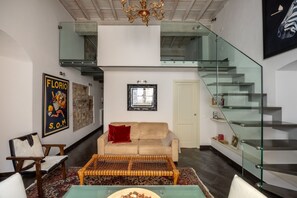 A modern living room with a sofa, a coffee table, a glass staircase, and a chandelier. - Calimaruzza Apartment - by Maison Florence (Firenze)