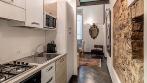 A modern kitchen with a gas stove, a microwave, and a sink. There is a dining area with a chair and a rug. A stone wall and a framed mirror are visible. - Calimaruzza Apartment - by Maison Florence (Firenze)