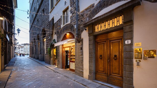 A cobblestone street with historic buildings, a shop with a wooden door, and string lights. - Calimaruzza Apartment - by Maison Florence (Firenze)